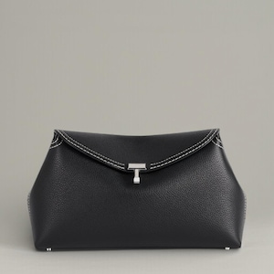 Pu&ograve; includere: Una pochette in pelle nera con chiusura a patta e cuciture bianche. La pochette presenta una chiusura color argento e una superficie strutturata. Il design &egrave; minimalista ed elegante, adatto a varie occasioni.