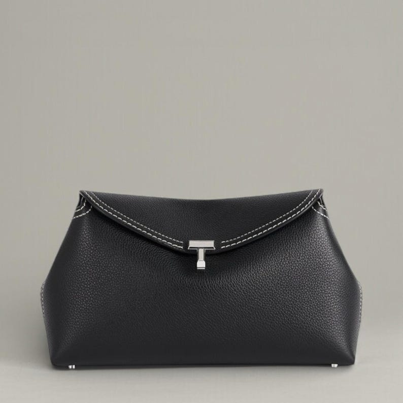 Pu&ograve; includere: Una pochette in pelle nera con chiusura a patta e cuciture bianche. La pochette presenta una chiusura color argento e una superficie strutturata. Il design &egrave; minimalista ed elegante, adatto a varie occasioni.