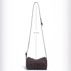 Puede incluir: Un bolso de hombro tejido de color marr&oacute;n oscuro con una correa larga y fina. La longitud de la correa se indica como 49-53 cm. El bolso tiene un cierre de cremallera y una forma cil&iacute;ndrica. El bolso est&aacute; hecho de un material tejido.