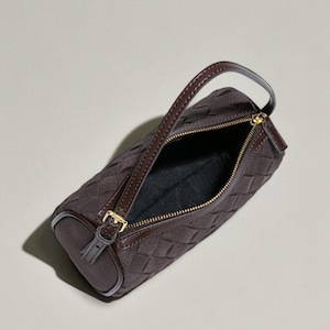 Puede incluir: Un bolso marr&oacute;n con un patr&oacute;n tejido y forma cil&iacute;ndrica. El bolso presenta un asa superior, una cremallera dorada y una hebilla dorada. El interior es negro. El bolso est&aacute; hecho de un material suave similar al ante.