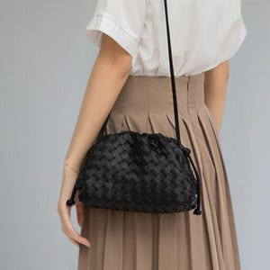 May include: A black woven leather crossbody bag with a drawstring closure. The bag has a long, thin strap and a rounded shape. The woven pattern is visible across the entire surface of the bag.