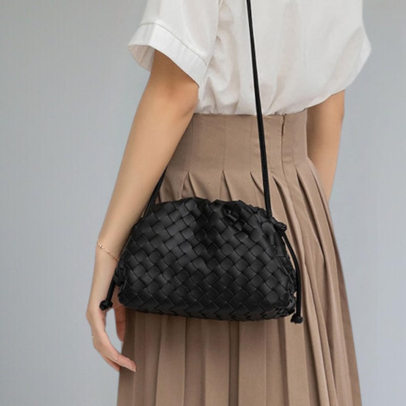 May include: A black woven leather crossbody bag with a drawstring closure. The bag has a long, thin strap and a rounded shape. The woven pattern is visible across the entire surface of the bag.