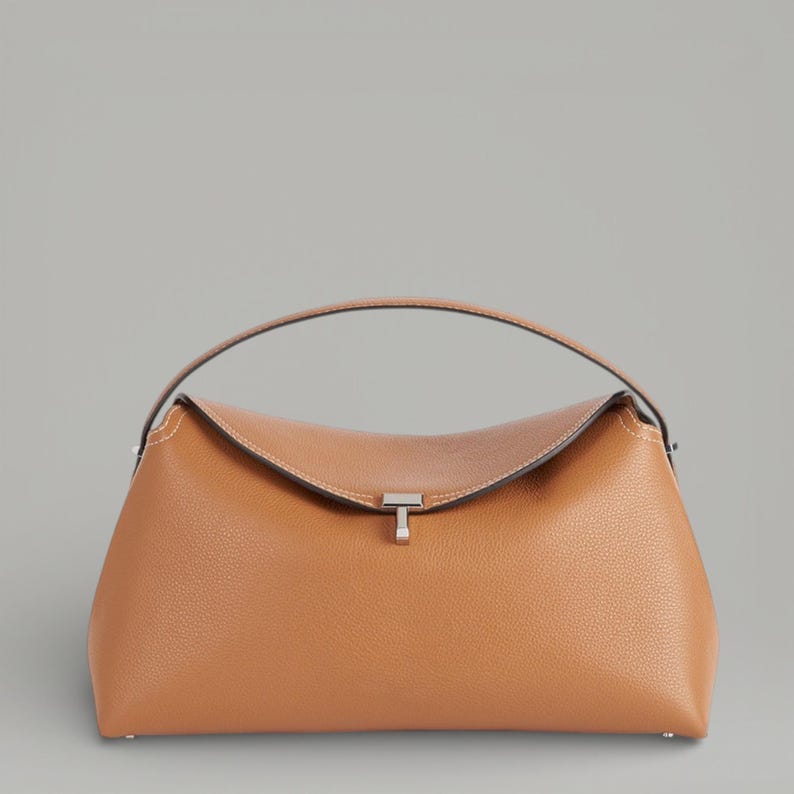 Pu&ograve; includere: Una borsa in pelle marrone chiaro con la parte superiore curva e un manico. La borsa ha una chiusura color argento e cuciture bianche lungo i bordi. La borsa &egrave; di medie dimensioni e ha una forma strutturata.