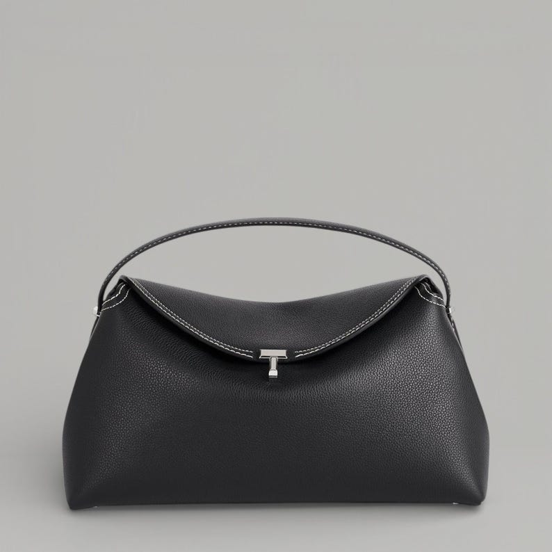 Pu&ograve; includere: Una borsa nera con la parte superiore curva e un piccolo manico. La borsa presenta cuciture bianche lungo i bordi e una chiusura color argento. La borsa &egrave; realizzata in un materiale strutturato.