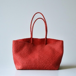 May include: A red woven tote bag with two braided handles. The bag has a rectangular shape and a wide opening. The woven material has a textured appearance. The bag is designed for carrying items.