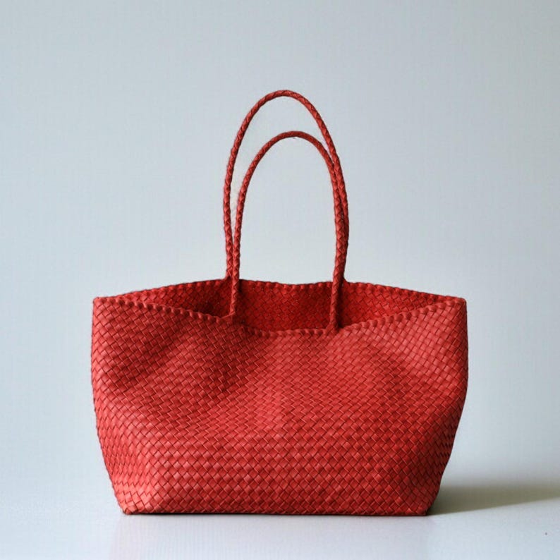 May include: A red woven tote bag with two braided handles. The bag has a rectangular shape and a wide opening. The woven material has a textured appearance. The bag is designed for carrying items.