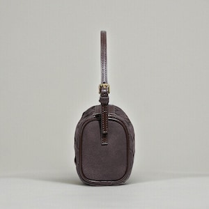 Puede incluir: Un bolso marr&oacute;n oscuro con un patr&oacute;n tejido y un asa corta. El bolso tiene forma rectangular con bordes redondeados y una hebilla dorada. El asa est&aacute; sujeta a la parte superior del bolso con una correa de cuero.