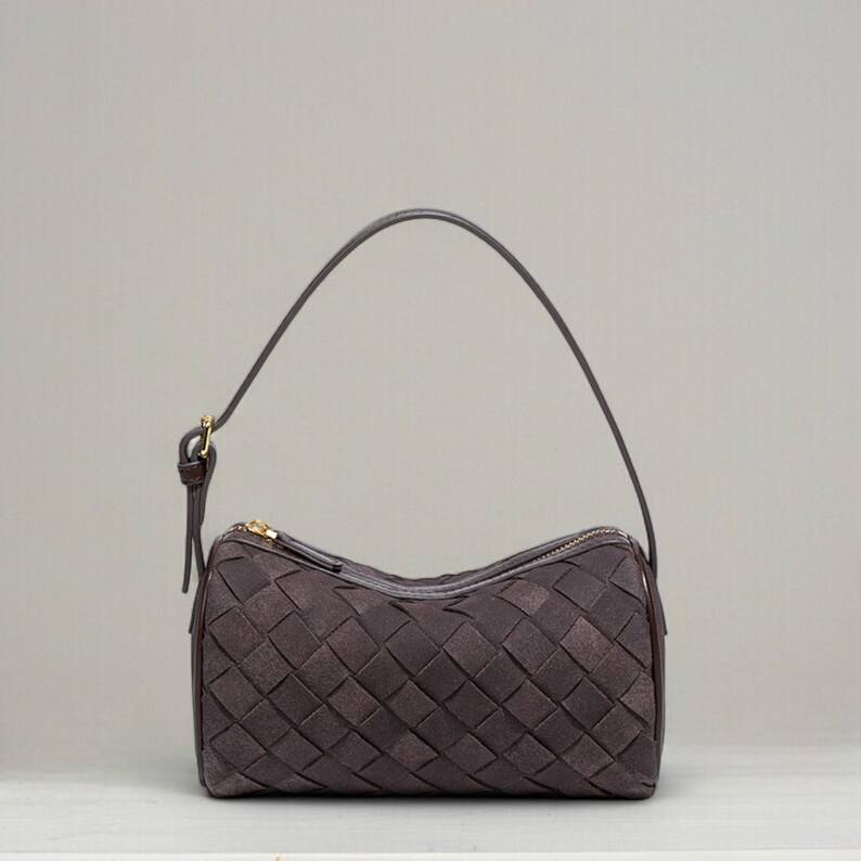 Puede incluir: Un bolso tejido marr&oacute;n oscuro con cremallera dorada y asa a juego. El bolso tiene forma rectangular y un patr&oacute;n tejido. El asa es fina y se sujeta al bolso con un peque&ntilde;o cierre dorado.