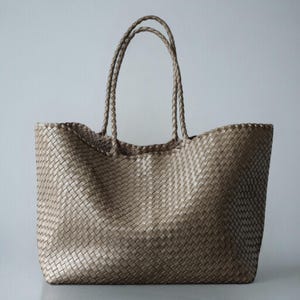 May include: A large, woven tote bag in a neutral beige color. The bag features two braided handles and a spacious interior. The woven pattern creates a textured surface, and the bag is designed for carrying items.