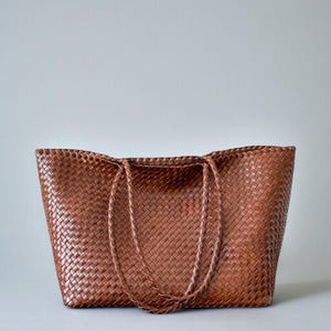 May include: A brown woven tote bag with braided handles. The bag is made of a tightly woven material, creating a textured surface. The bag is rectangular with a wide opening and is suitable for carrying various items.