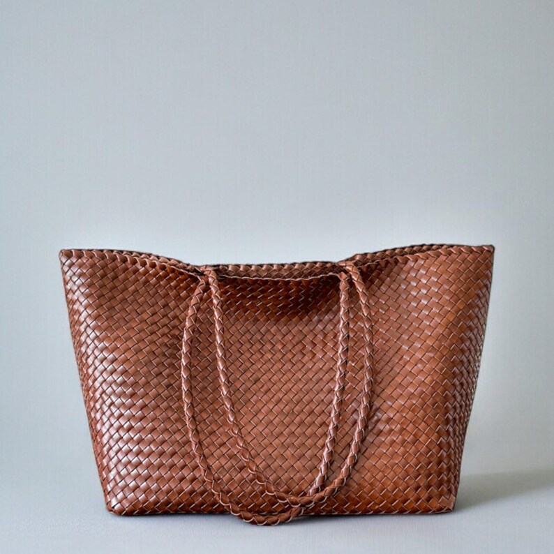 May include: A brown woven tote bag with braided handles. The bag is made of a tightly woven material, creating a textured surface. The bag is rectangular with a wide opening and is suitable for carrying various items.