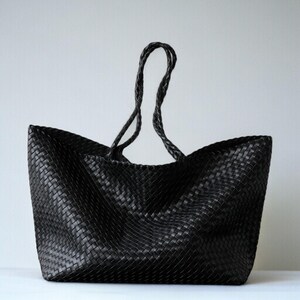 May include: A black woven tote bag with braided handles. The bag has a rectangular shape with a wide opening and a textured surface. The handles are long enough to be worn over the shoulder.