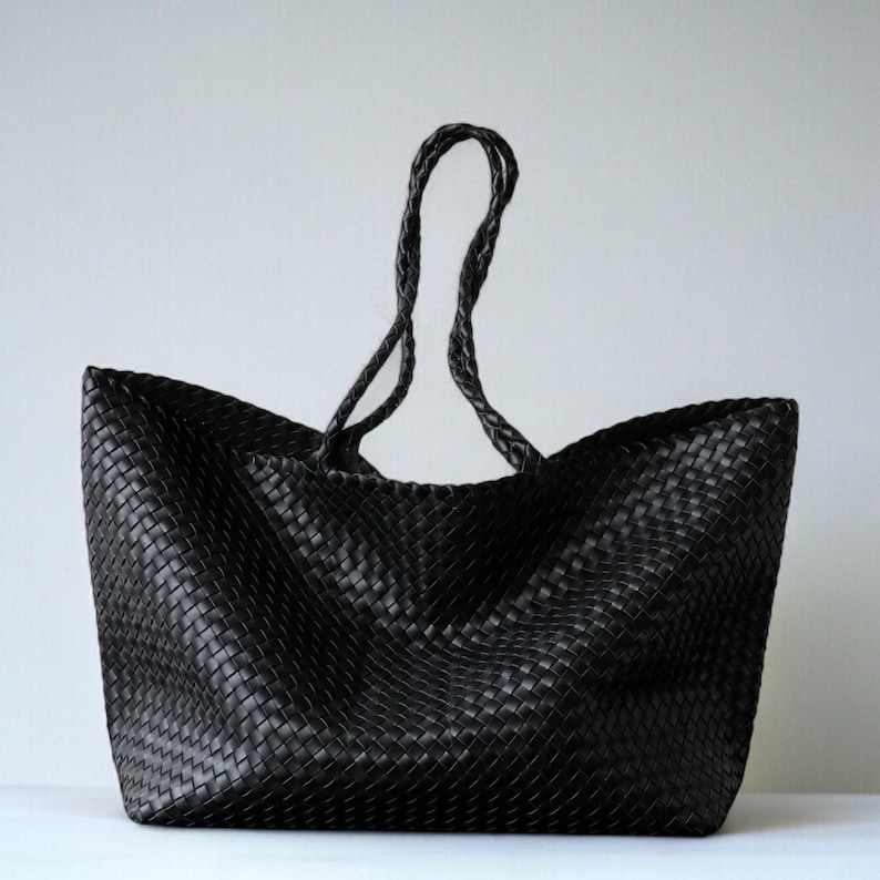 May include: A black woven tote bag with braided handles. The bag has a rectangular shape with a wide opening and a textured surface. The handles are long enough to be worn over the shoulder.