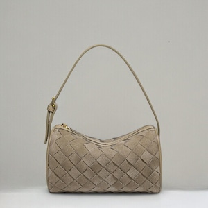 Puede incluir: Un bolso beige con un dise&ntilde;o tejido. El bolso tiene forma cil&iacute;ndrica con un asa superior y una cremallera dorada. El patr&oacute;n tejido est&aacute; hecho de piezas rectangulares de material.