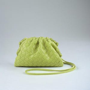 May include: A lime green clutch bag with a woven pattern. The bag features a gathered top and a thin, matching strap. The bag is made of a soft material and is set against a plain white background.