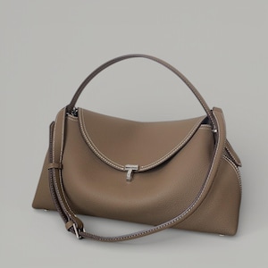 Pu&ograve; includere: Borsa a mano color talpa con patta superiore curva e chiusura argentata. Presenta un manico superiore e una tracolla staccabile. Le cuciture bianche accentuano i bordi, creando un contrasto. Realizzata in materiale strutturato.