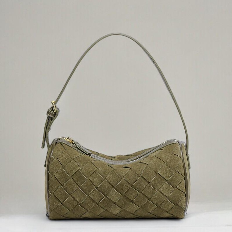 Puede incluir: Bolso de mano de ante verde oliva con dise&ntilde;o tejido. El bolso tiene forma cil&iacute;ndrica, cierre de cremallera y una sola correa para el hombro. Los herrajes son dorados.