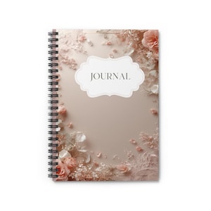Peut inclure: Un journal à spirale avec un motif floral. La couverture présente un fond rose clair avec des fleurs roses et blanches éparpillées. Le mot "JOURNAL" est dans un cadre blanc décoratif.