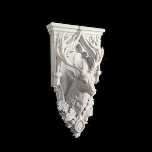 May include: A white wall-mounted decorative corbel featuring a sculpted deer head with large antlers. The piece is framed by an arched architectural structure and adorned with detailed oak leaves and acorns at the base, finished in a matte texture.