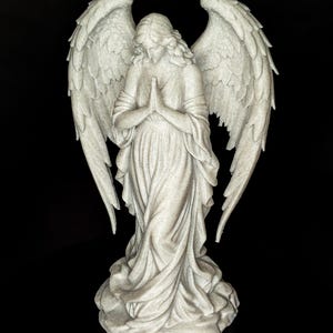 May include: A detailed statue of an angel with large, textured wings. The angel is depicted in a flowing gown, with hands clasped in prayer. The sculpture is a light gray color and stands on a textured base, set against a black background.
