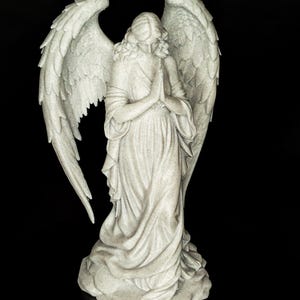 May include: A detailed statue of an angel with large, textured wings and flowing robes. The angel is depicted with hands clasped in prayer, and the sculpture has a speckled, off-white finish. The background is solid black.