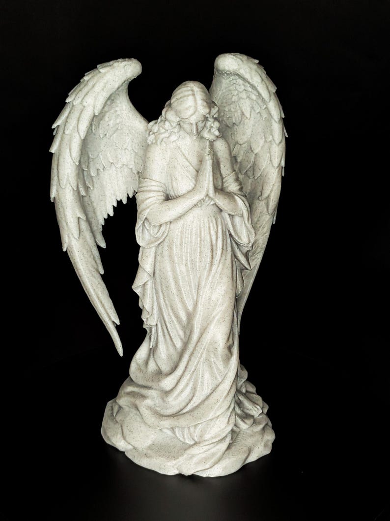 May include: A detailed statue of an angel with large, textured wings and flowing robes. The angel is depicted with hands clasped in prayer, and the sculpture has a speckled, off-white finish. The background is solid black.