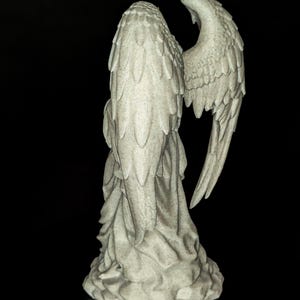 May include: A detailed, off-white angel statue with outstretched wings. The statue is sculpted with intricate feather details and draped fabric. The angel is set against a black background, highlighting its form and texture.