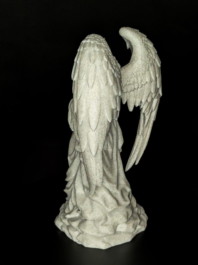 May include: A detailed, off-white angel statue with outstretched wings. The statue is sculpted with intricate feather details and draped fabric. The angel is set against a black background, highlighting its form and texture.