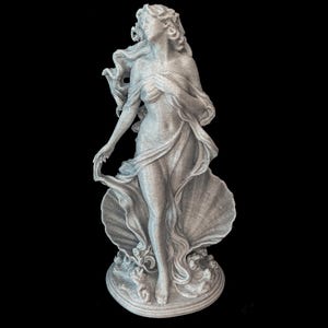 以下が含まれることがあります： 淡いグレーの斑点模様がある3Dプリント製のフィギュア。長い髪をなびかせ、布をまとった人物が立っている姿を表現しています。人物は大きな開いた貝殻の前に配置されており、円形の台座の土台部分には波の模様が施されています。