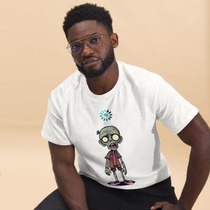 Peut inclure: T-shirt blanc avec un dessin de zombie de dessin animé et une icône de cerveau. Le zombie porte une veste et un short marron. Le design est de style cartoon.