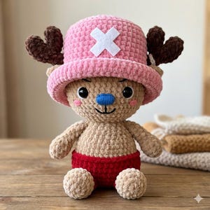 May include: A crocheted plush toy depicting a cartoon character. The toy features a tan body, red shorts, and a pink hat with a white cross. It has brown antlers, a blue nose, and black eyes. The toy is positioned on a wooden surface.