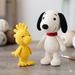Può includere: Due figure all'uncinetto di Snoopy e Woodstock. Snoopy è bianco con orecchie nere e un colletto rosso. Woodstock è giallo. Entrambe le figure sono su una superficie di legno. Le figure sono fatte a mano e sembrano giocattoli o oggetti da collezione.