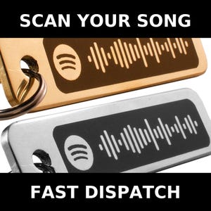 Op de afbeelding: Twee metalen sleutelhangers, één goudkleurig en één zilverkleurig, met Spotify-logo's en scanbare muziekcodes. De goudkleurige sleutelhanger heeft de tekst "SCAN YOUR SONG" erboven. De zilverkleurige sleutelhanger heeft de tekst "FAST DISPATCH" eronder.