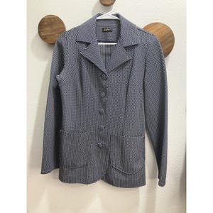 May include: A navy blue and white patterned blazer with a notched collar, long sleeves, and two front pockets. The blazer has a three-button closure and is hanging on a white hanger.