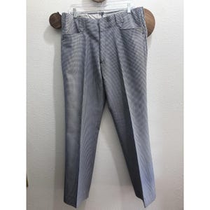 May include: A pair of trousers featuring a fine black and white micro-check pattern. The pants include a structured waistband with belt loops, a front zipper fly, and two side pockets. The fabric has a consistent, small-scale geometric grid design.