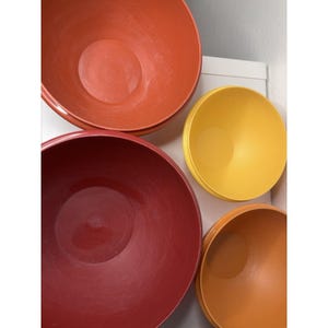 Può includere: Una collezione di quattro ciotole colorate per mescolare in tonalità di rosso, arancione e giallo. Le ciotole sono disposte in una configurazione nidificata, con la ciotola più grande in una tonalità rosso intenso e la più piccola in un giallo brillante.