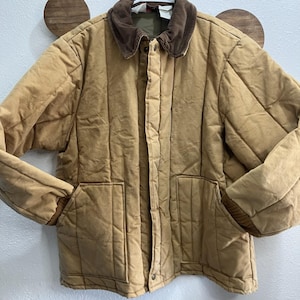 May include: A tan quilted jacket with a brown corduroy collar and two front pockets. The jacket has a button-up front and ribbed cuffs. The jacket is a neutral colour and suitable for various outfits.