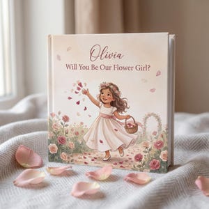 Puede incluir: Un libro de tapa dura con una cubierta de color crema que presenta el nombre Olivia y el texto Will You Be Our Flower Girl? La ilustración muestra a un niño con un vestido blanco y una faja rosa, usando una corona de flores y lanzando pétalos.