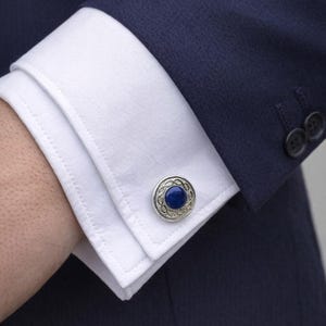 May include: A white ceramic mug with a black handle and the text "But First, Coffee" in a bold, black font. The mug is set against a blurred background, highlighting its clean design.