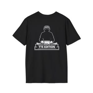 May include: Black t-shirt featuring a white graphic of a person at a DJ setup. The person is wearing a hat with the text "FAAFO". Below the person is the text "TTE EDITION" in a rectangular frame.