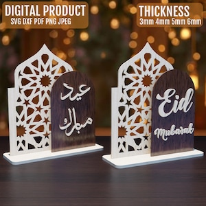 Può includere: Due decorazioni in legno Eid Mubarak. Ognuna ha un design ad arco tagliato al laser bianco con un motivo a stella. Una ha testo arabo, l'altra dice "Eid Mubarak". La base è bianca, il testo su sfondo in legno scuro.