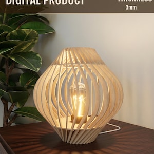 Può includere: Una lampada da tavolo in legno con un design unico a doghe aperte. La lampada ha una finitura in legno naturale e una lampadina visibile. Il testo "DIGITAL PRODUCT" e "THICKNESS 3mm" sono visibili. La lampada è su una superficie marrone scuro.