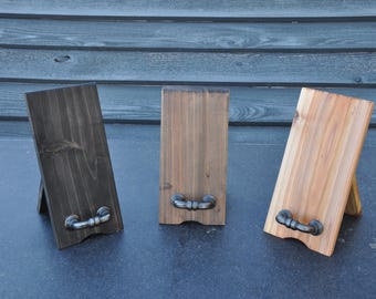 May include: Three wooden display stands in varying shades of brown. Each stand has a rectangular shape with a metal handle at the bottom. The stands are angled, resting on a small wooden support.