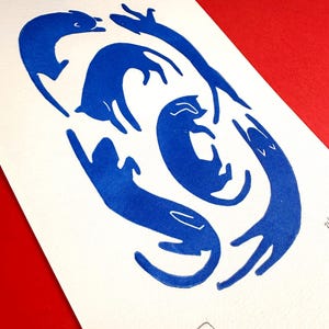 May include: A print featuring stylized blue cats in various playful poses on white paper. The cats are arranged in a circular pattern, with some stretching and others curled up. The background is a solid red.