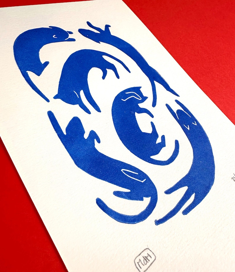 May include: A print featuring stylized blue cats in various playful poses on white paper. The cats are arranged in a circular pattern, with some stretching and others curled up. The background is a solid red.