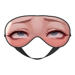 Op de afbeelding: Een zwart slaapmasker met een gedetailleerde illustratie van een gezicht. Het masker heeft blauwe ogen, lange wimpers en blozende wangen. Het heeft een zwarte band. Het ontwerp is artistiek en opvallend.
