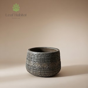 May include: A gray, round planter with a textured, geometric pattern. The planter has a wide opening and a dark interior. The Leaf Habitat logo is in the upper left corner. This decorative planter is suitable for indoor or outdoor use.
