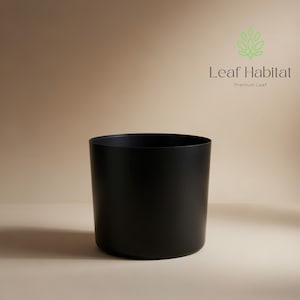 Puede incluir: Una maceta cilíndrica negra mate. La maceta está vacía y lista para plantas. El logotipo de Leaf Habitat es visible en la esquina superior derecha. La maceta está hecha de un material sólido y tiene una superficie lisa.