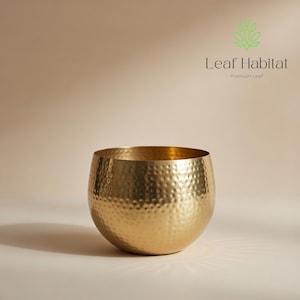 May include: A gold-coloured, hammered metal bowl with a rounded shape. The bowl has a textured surface and is designed for decorative purposes. The Leaf Habitat logo is in the upper right corner.