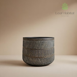 May include: A dark grey ceramic planter with a textured, geometric design. The planter features horizontal bands of parallel lines and diagonal stripes. The rim is a solid dark grey, and the overall shape is cylindrical.